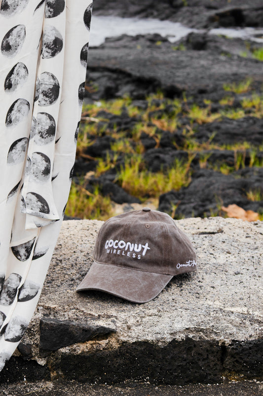 Close-up of the Coconut Ave Dad Hat in Coconut Wireless Vintage Black resting on volcanic rocks, showcasing the embroidered Coconut Wireless logo and vintage washed cotton fabric.