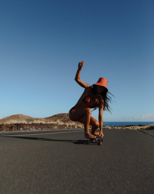 Woman skateboarding along a coastal road in island-inspired fashion, capturing the adventurous lifestyle and creative spirit of the Coconut Ave Brand Ambassador Program.