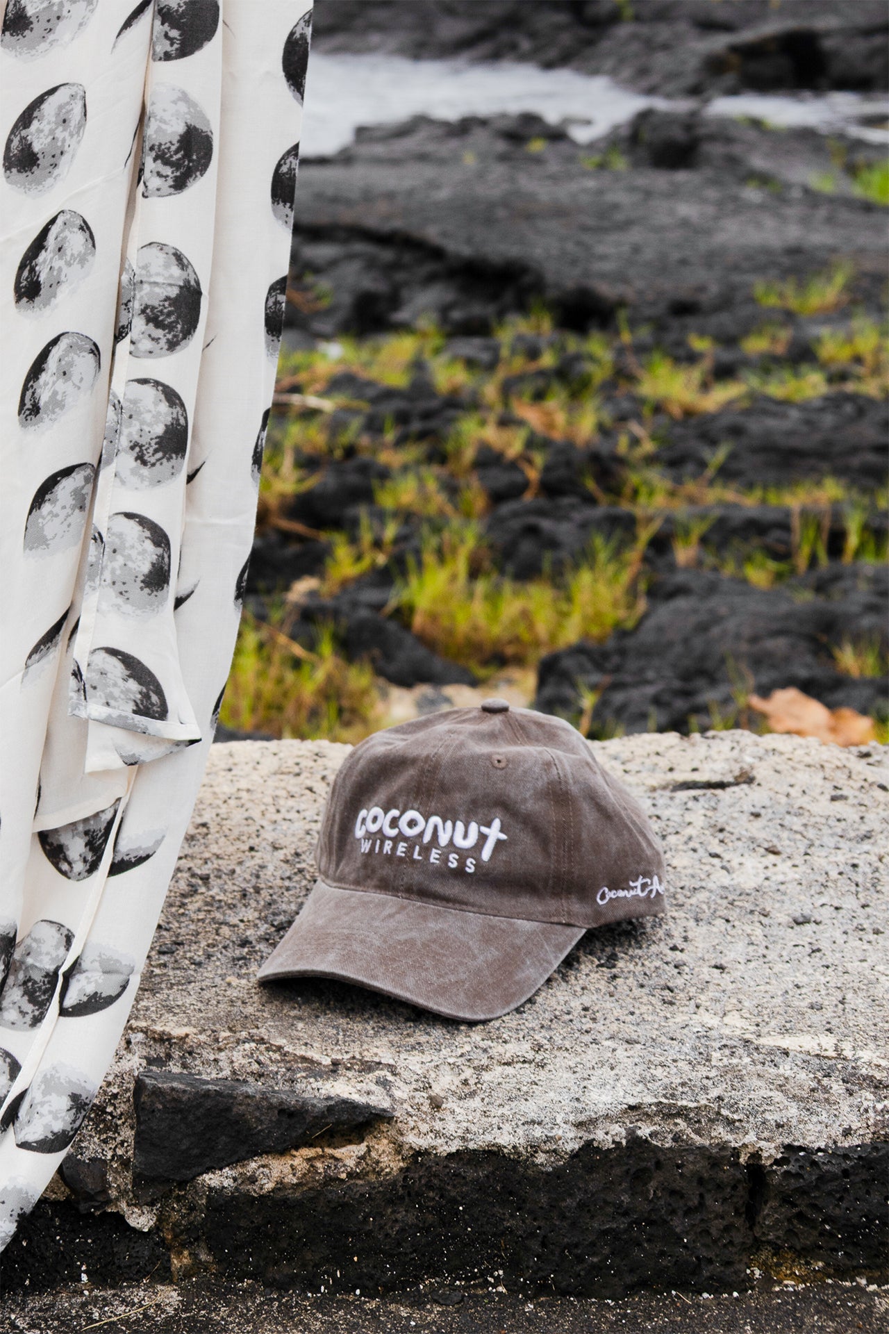 Close-up of the Coconut Ave Dad Hat in Coconut Wireless Vintage Black resting on volcanic rocks, showcasing the embroidered Coconut Wireless logo and vintage washed cotton fabric.
