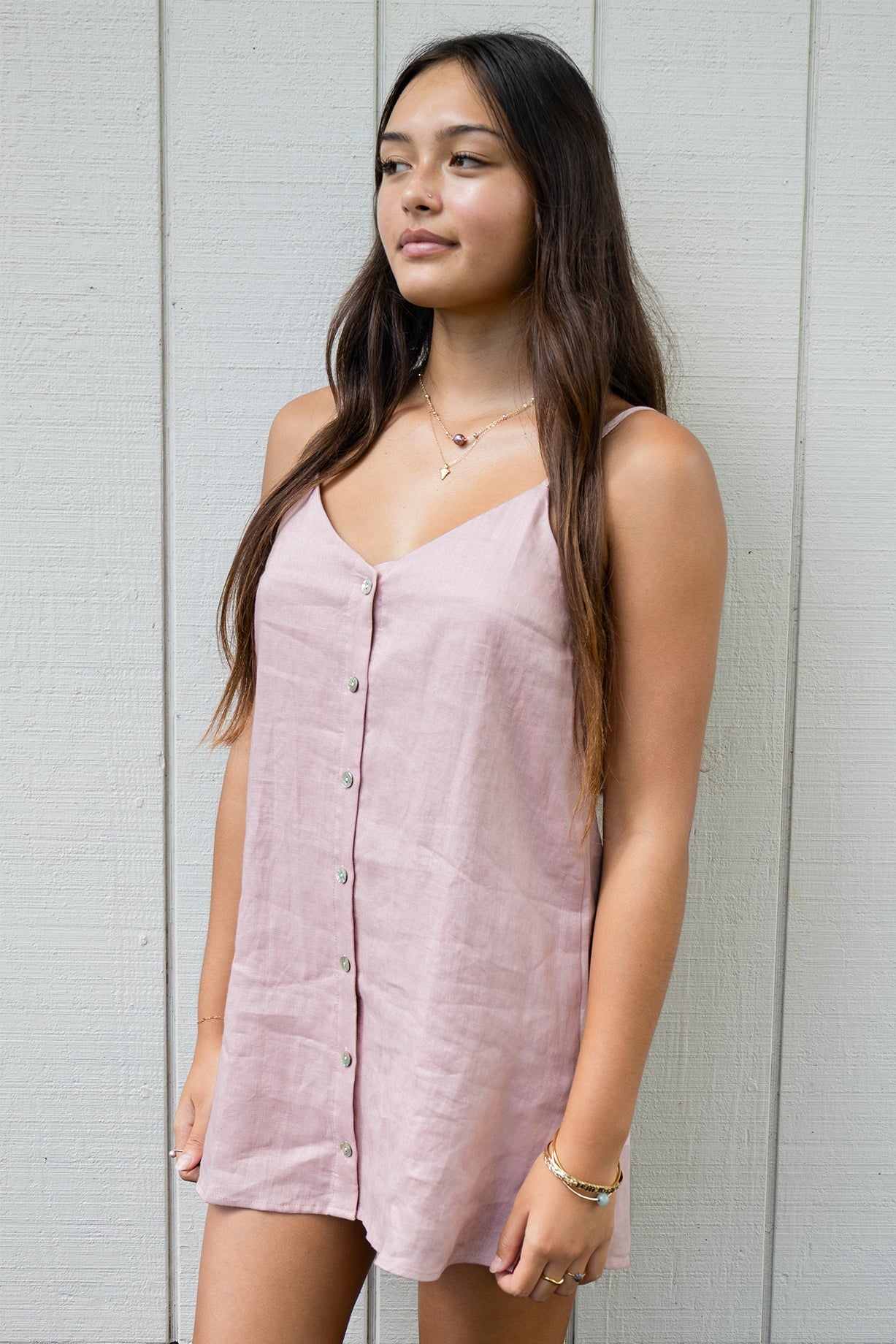 Model wearing the Coconut Ave Day Tripper Dress in Rosey, a sleeveless linen mini dress with adjustable straps and a mother-of-pearl button placket.