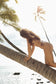 Woman modeling the Hula Triangle Top in Chocolate Bloom on a tropical beach beneath palm trees