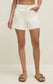 Model wearing the Jonah Mid-Rise Short in Cloud with a white tank top and sandals for a casual warm-weather outfit.