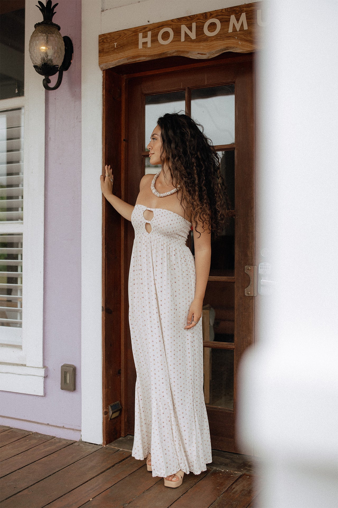 Mau'umae Maxi Dress in Puka Shell styled with sandals for relaxed resort wear on a tropical porch.