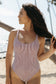 Side view of a woman wearing the Bamboo Chocolate Skipper One Piece Swimsuit on the beach