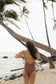 Side view of a woman wearing the Stevie One Piece in Chocolate Bloom in a tropical beach setting