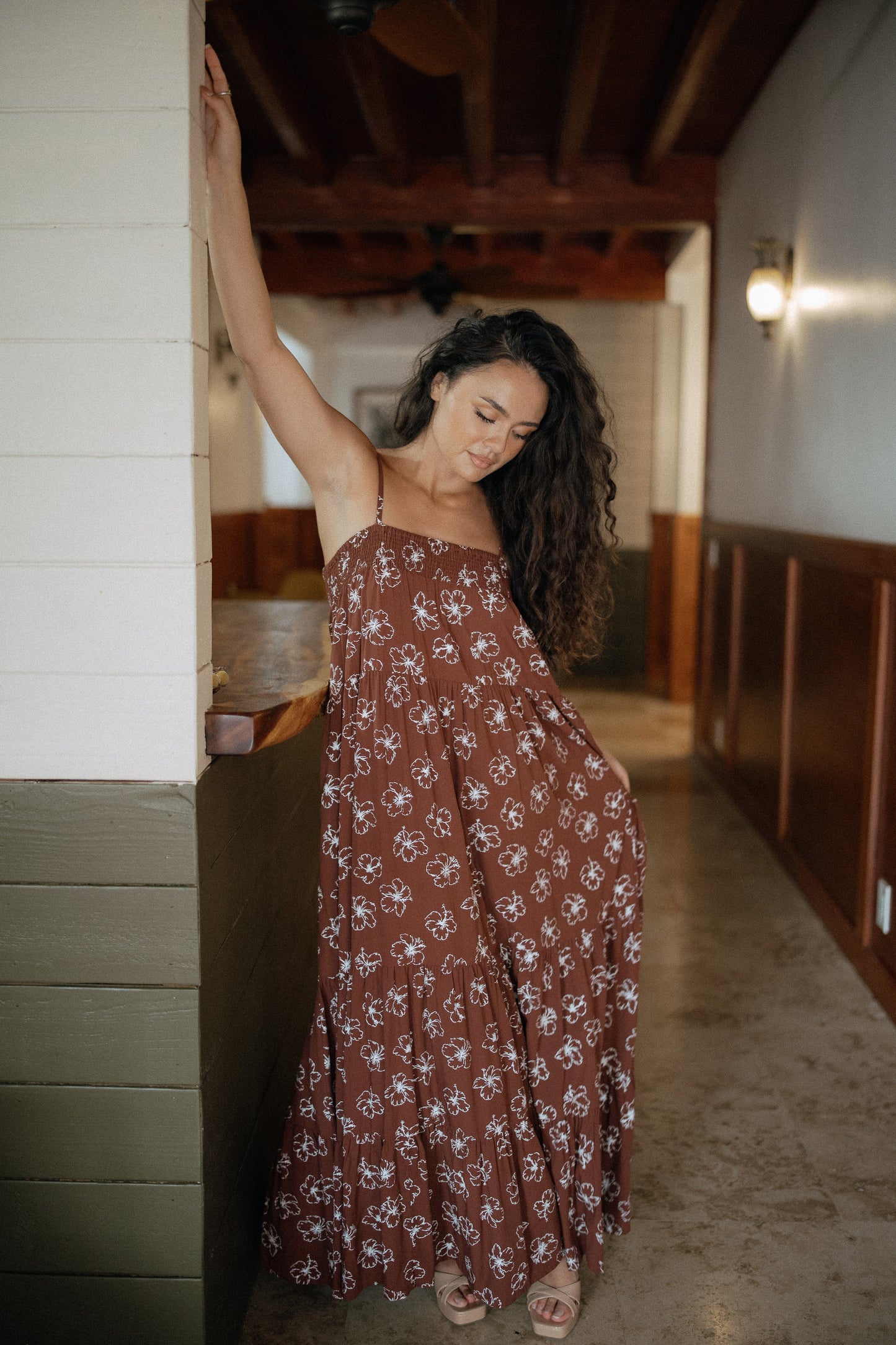 Waikiki Maxi Dress in Chocolate Bloom styled for tropical resort wear in a warm wood interior.