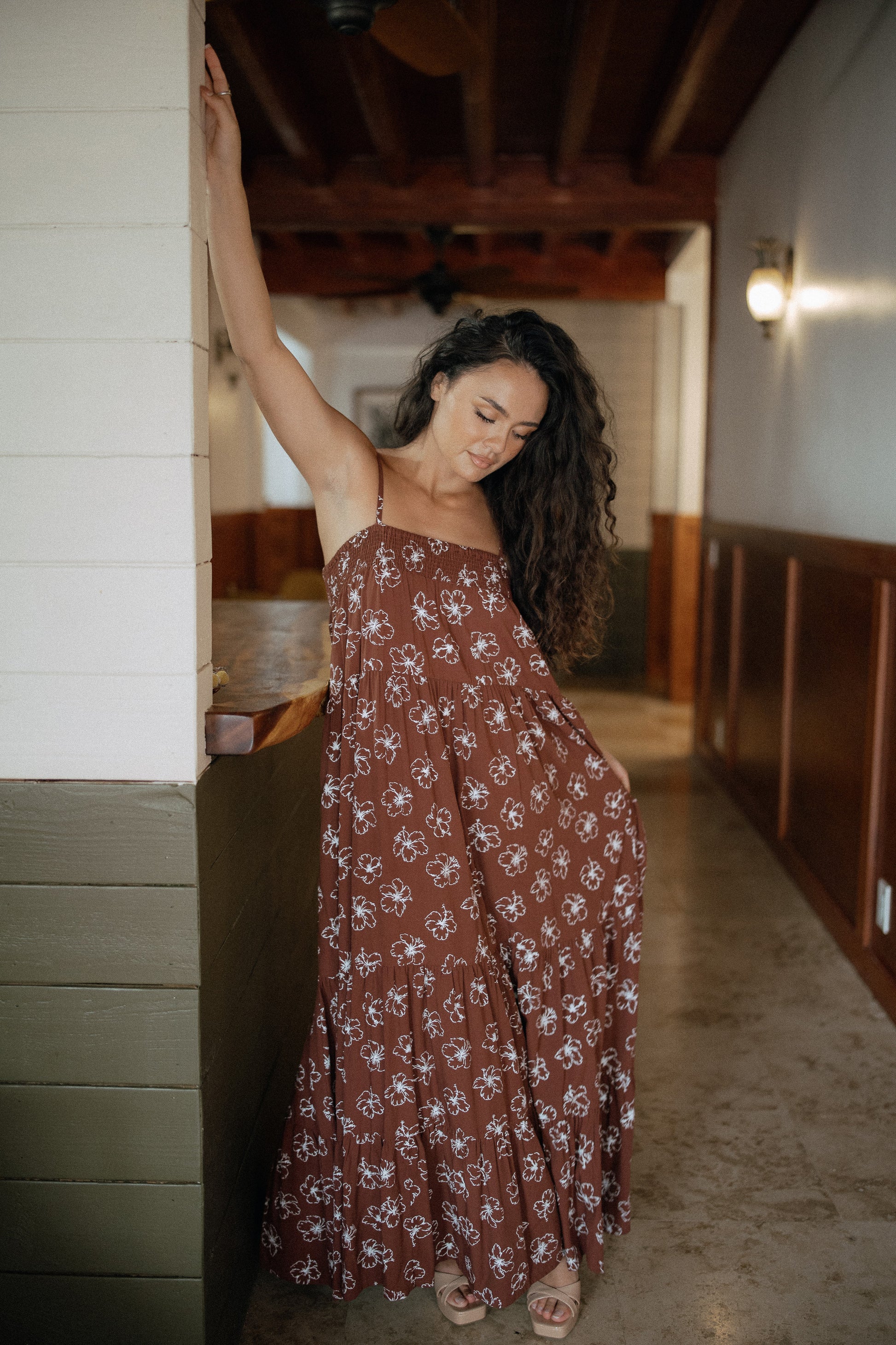 Waikiki Maxi Dress in Chocolate Bloom styled for tropical resort wear in a warm wood interior.