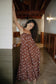Waikiki Maxi Dress in Chocolate Bloom styled for tropical resort wear in a warm wood interior.