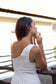 Back view of a woman wearing the Coconut Ave Jane Dress in Natural featuring the one-shoulder design, smocked back, and breathable midi dress silhouette.