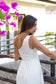 Back view of a woman wearing the Coconut Ave Jane Dress in Natural showcasing the one-shoulder silhouette, smocked bodice, and lightweight crepe fabric.