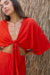 Woman wearing the Coconut Ave Tulum Top in Hibiscus showcasing the adjustable tie-front closure, relaxed drape, and matching resort wear skirt.